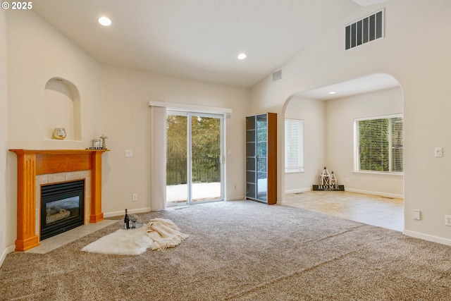 unfurnished living room featuring lofted ceiling, plenty of natural light, light colored carpet, and a tiled fireplace