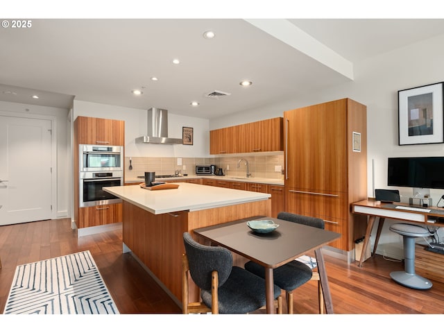 kitchen featuring wall chimney range hood, brown cabinetry, visible vents, modern cabinets, and a sink