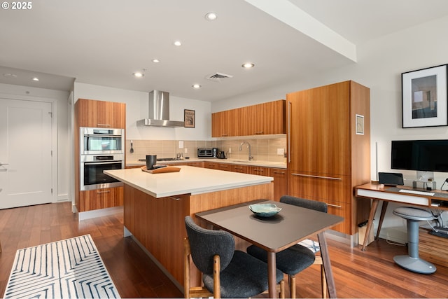 311 NW 12th Ave Unit 603, Portland, OR 97209 - kitchen featuring wall chimney range hood, brown cabinetry, visible vents, modern cabinets, and a sink