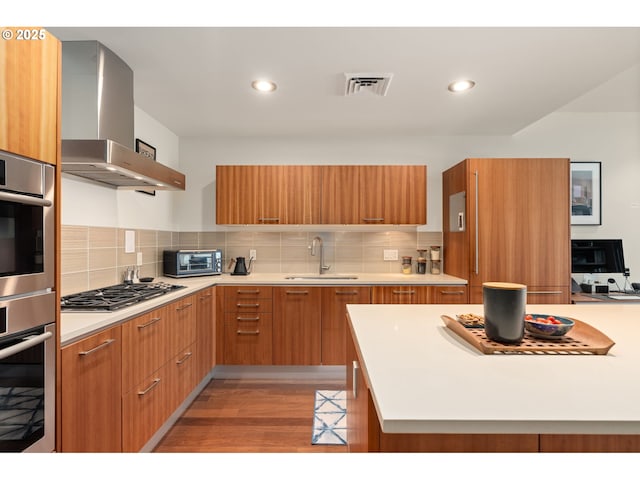 kitchen featuring a sink, wall chimney exhaust hood, stainless steel appliances, visible vents, and modern cabinets
