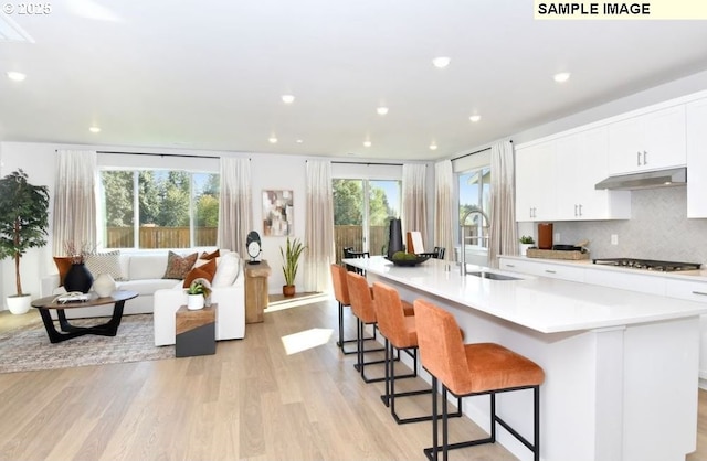 kitchen with light wood-type flooring, under cabinet range hood, tasteful backsplash, a sink, and stainless steel gas stovetop