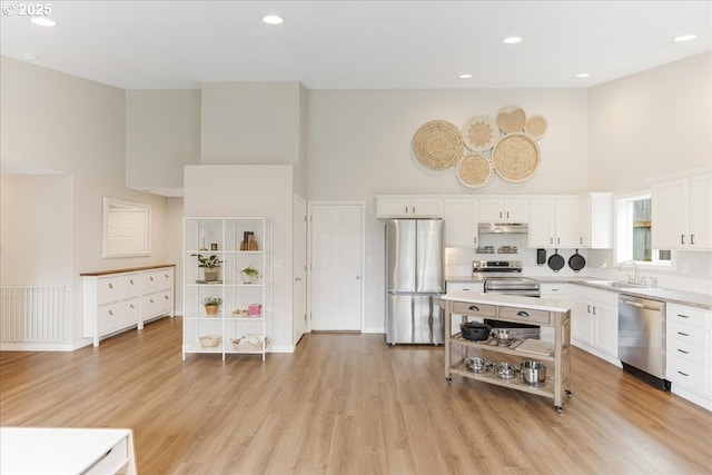 kitchen with white cabinets, a high ceiling, light countertops, stainless steel appliances, and under cabinet range hood