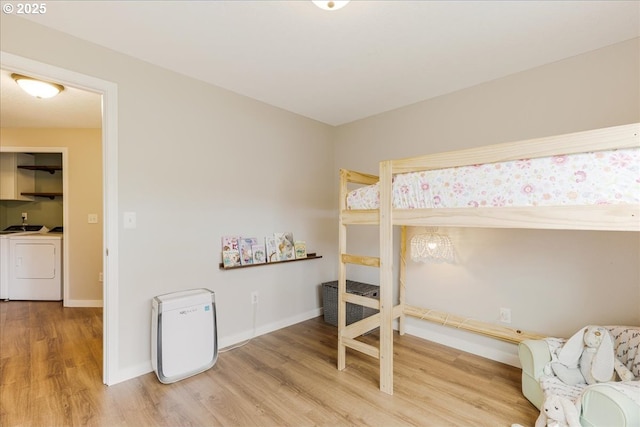 bedroom featuring baseboards, washer and clothes dryer, and light wood finished floors