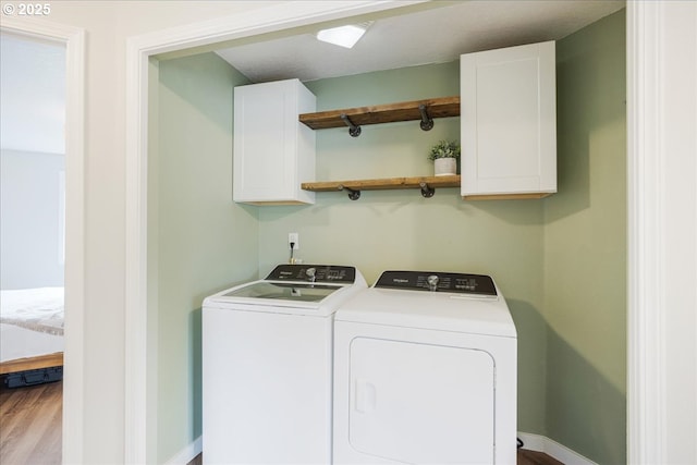 laundry area featuring baseboards, cabinet space, wood finished floors, and washing machine and clothes dryer