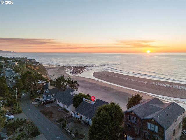 aerial view at dusk featuring a water view and a beach view