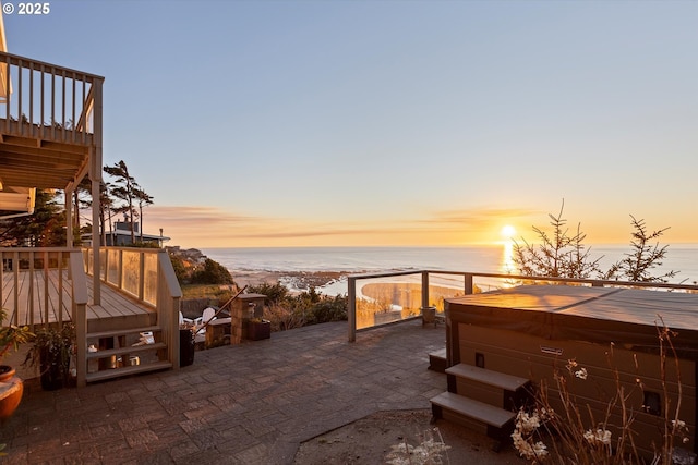 patio terrace at dusk with a deck with water view, a beach view, and a hot tub