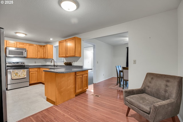 6410 SW 204th Pl, Beaverton, OR 97078 - kitchen featuring stainless steel appliances, a peninsula, dark countertops, light wood-type flooring, and a textured ceiling