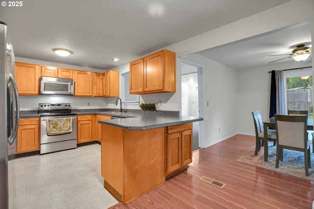 6410 SW 204th Pl, Beaverton, OR 97078 - kitchen with stainless steel appliances, a peninsula, dark countertops, ceiling fan, and light wood-style flooring