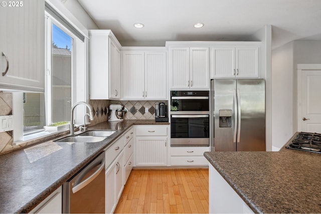 7540 SW Becky Ct, Beaverton, OR 97007 - kitchen with stainless steel appliances, a sink, white cabinets, light wood-style floors, and tasteful backsplash