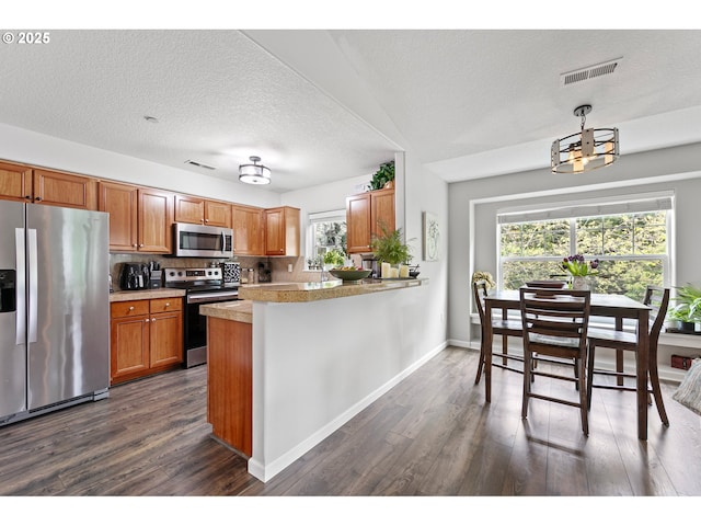 kitchen with brown cabinets, stainless steel appliances, visible vents, and dark wood-style flooring