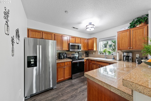kitchen featuring a sink, tile counters, brown cabinetry, and stainless steel appliances
