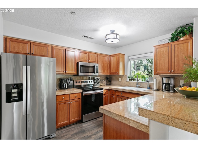 kitchen featuring brown cabinets, appliances with stainless steel finishes, a sink, tile countertops, and dark wood-type flooring