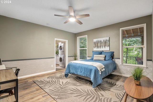 bedroom with wood-type flooring, ceiling fan, multiple windows, stacked washer and clothes dryer, and ensuite bath