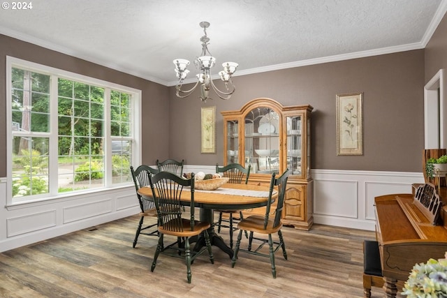 dining room with wood-type flooring, an inviting chandelier, a textured ceiling, and ornamental molding