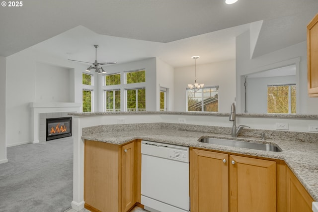 kitchen featuring light carpet, dishwasher, ceiling fan with notable chandelier, a tile fireplace, and sink