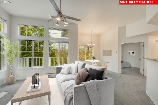 living room with ceiling fan with notable chandelier, light colored carpet, a baseboard heating unit, and a towering ceiling