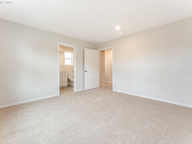 unfurnished bedroom featuring light carpet and connected bathroom