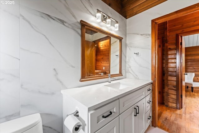 bathroom featuring log walls, wood finished floors, vanity, and toilet