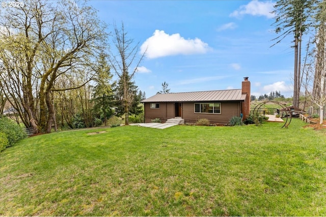 rear view of property with a chimney, a standing seam roof, metal roof, and a lawn