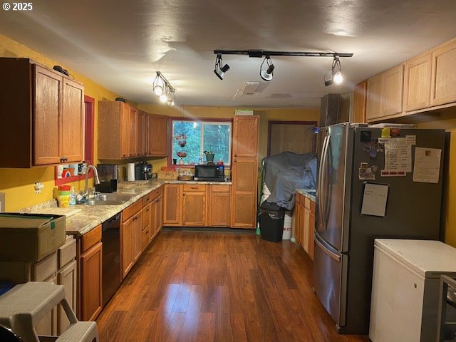 kitchen with a sink, black dishwasher, freestanding refrigerator, light countertops, and dark wood-style flooring