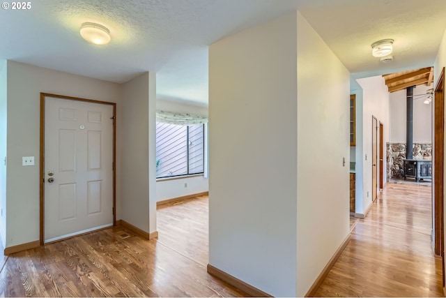 17708 SW Meadowbrook Way, Beaverton, OR 97078 - foyer entrance featuring light wood-type flooring, baseboards, a wood stove, and a textured ceiling