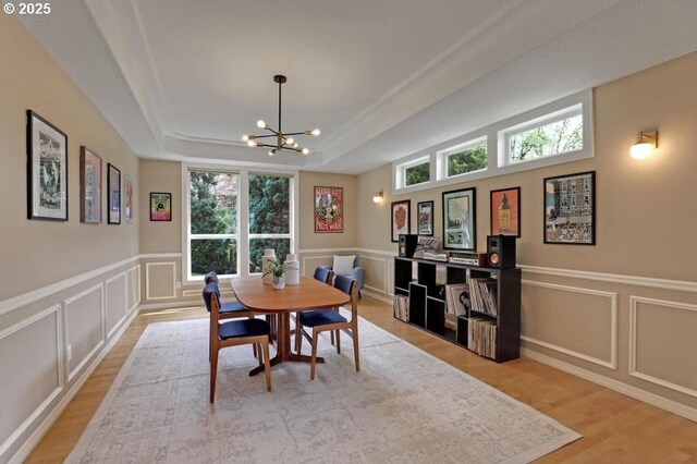 dining area with an inviting chandelier, a raised ceiling, a decorative wall, and light wood-type flooring