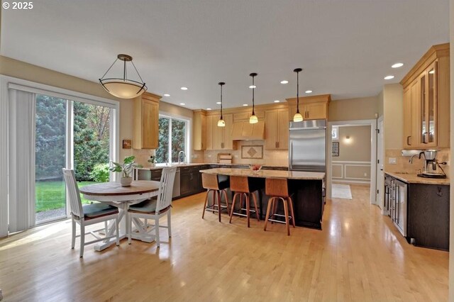 kitchen with a kitchen island, stainless steel built in fridge, tasteful backsplash, light stone counters, and light wood finished floors