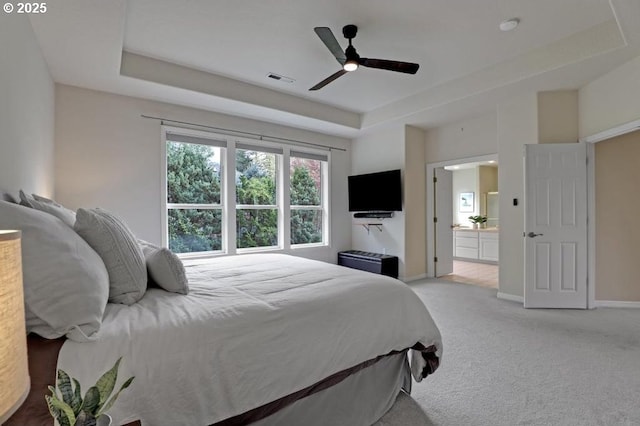 bedroom with light carpet, baseboards, ensuite bathroom, a tray ceiling, and visible vents