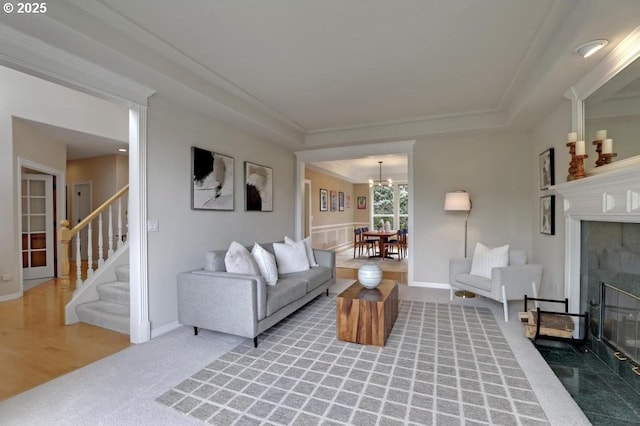 living area with crown molding, light colored carpet, a notable chandelier, stairs, and a tile fireplace