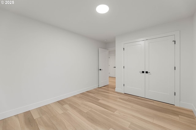 unfurnished bedroom with a closet, baseboards, and light wood-style flooring