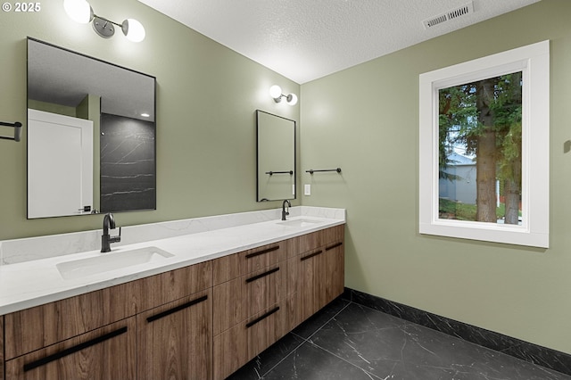 full bathroom with visible vents, a textured ceiling, baseboards, and a sink