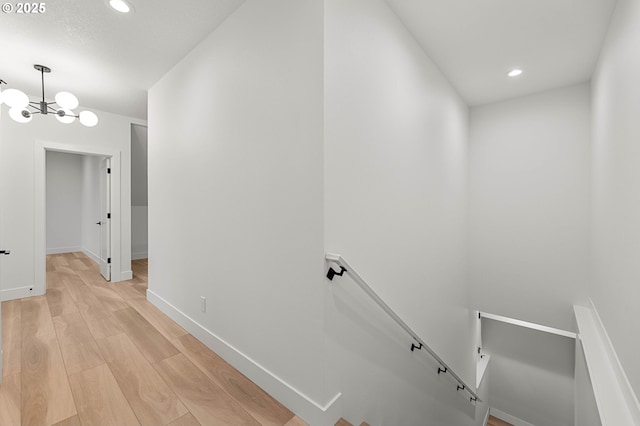 corridor with light wood finished floors, baseboards, an upstairs landing, recessed lighting, and a notable chandelier