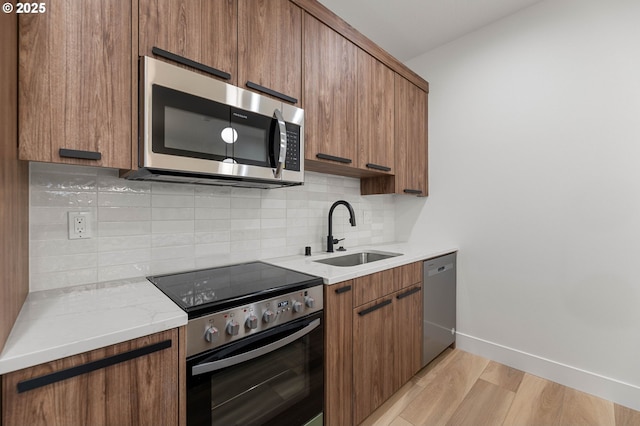 kitchen featuring tasteful backsplash, baseboards, light wood-style floors, stainless steel appliances, and a sink