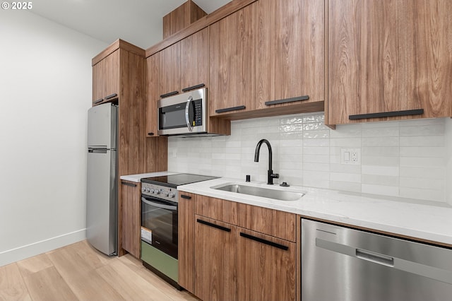 kitchen featuring baseboards, decorative backsplash, brown cabinets, stainless steel appliances, and a sink