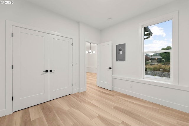 unfurnished bedroom featuring electric panel, a closet, light wood-type flooring, and baseboards