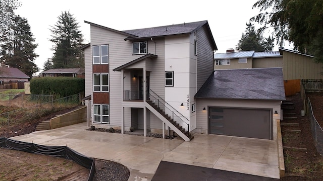 rear view of house featuring a garage, concrete driveway, stairs, and fence