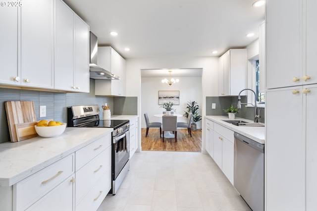 kitchen with backsplash, appliances with stainless steel finishes, white cabinets, a sink, and wall chimney exhaust hood