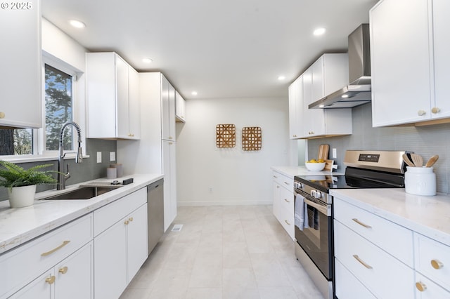 kitchen with wall chimney exhaust hood, appliances with stainless steel finishes, a sink, light stone countertops, and backsplash