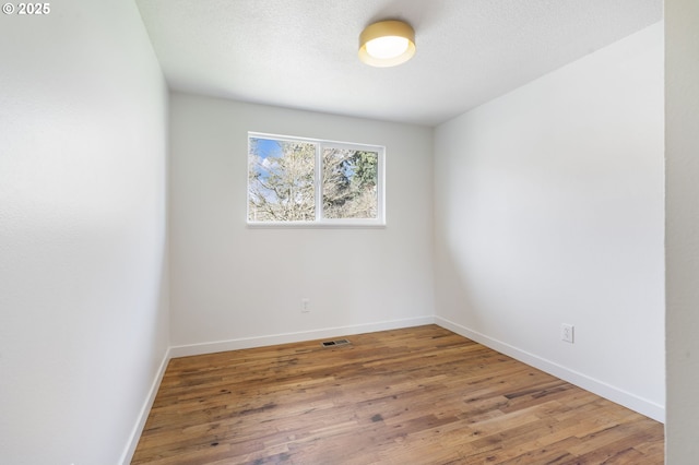 empty room with visible vents, a textured ceiling, baseboards, and wood finished floors