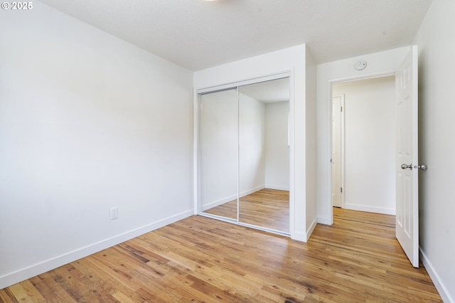 unfurnished bedroom with a closet, light wood-style flooring, and baseboards