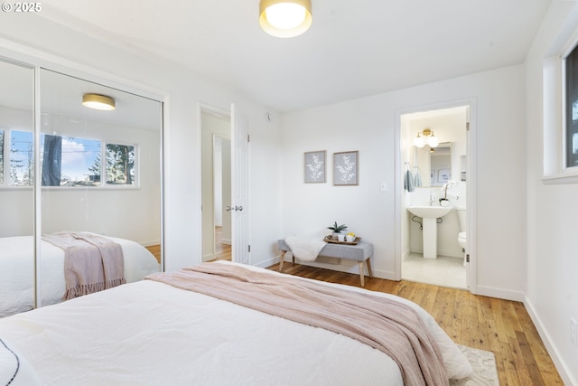 bedroom featuring light wood-style floors, baseboards, a closet, and ensuite bathroom