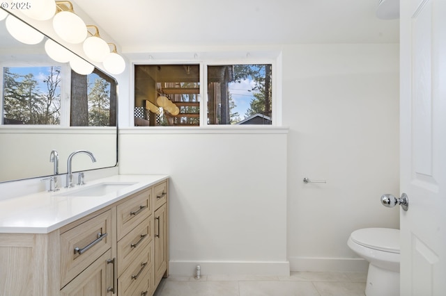 bathroom featuring toilet, a healthy amount of sunlight, vanity, baseboards, and tile patterned floors