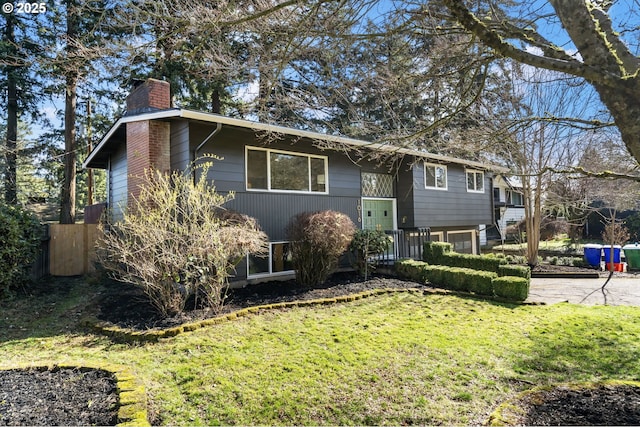 raised ranch with driveway, a chimney, and a front lawn