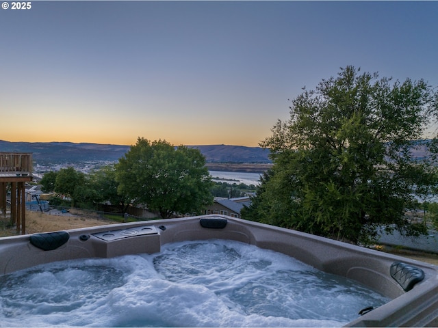 pool at dusk with a mountain view and a hot tub