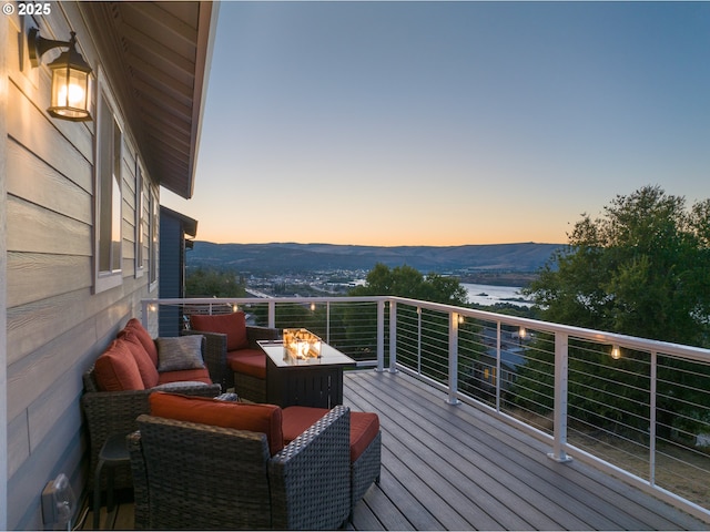 deck at dusk featuring a water and mountain view and an outdoor fire pit