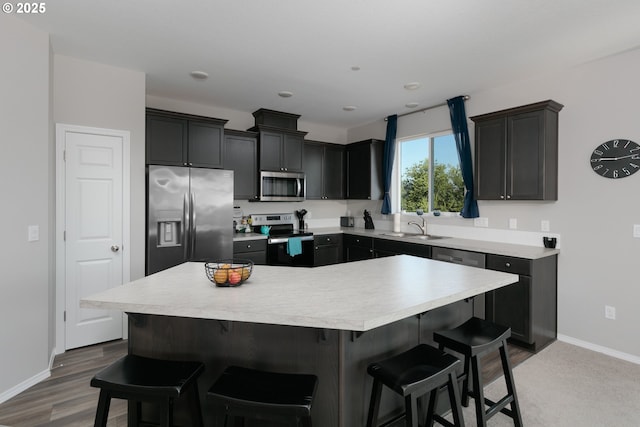 kitchen with a kitchen island, appliances with stainless steel finishes, sink, a breakfast bar area, and dark wood-type flooring