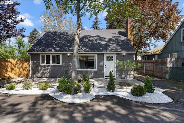 view of front facade featuring a chimney, fence, a patio, and roof with shingles