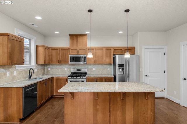 kitchen with pendant lighting, appliances with stainless steel finishes, a kitchen island, sink, and backsplash