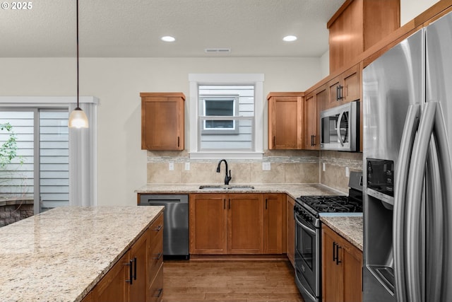 kitchen with backsplash, pendant lighting, sink, light stone countertops, and stainless steel appliances