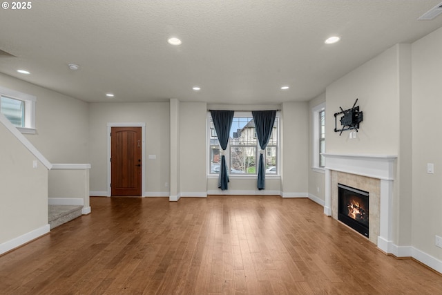 unfurnished living room featuring a textured ceiling, hardwood / wood-style floors, and a tiled fireplace